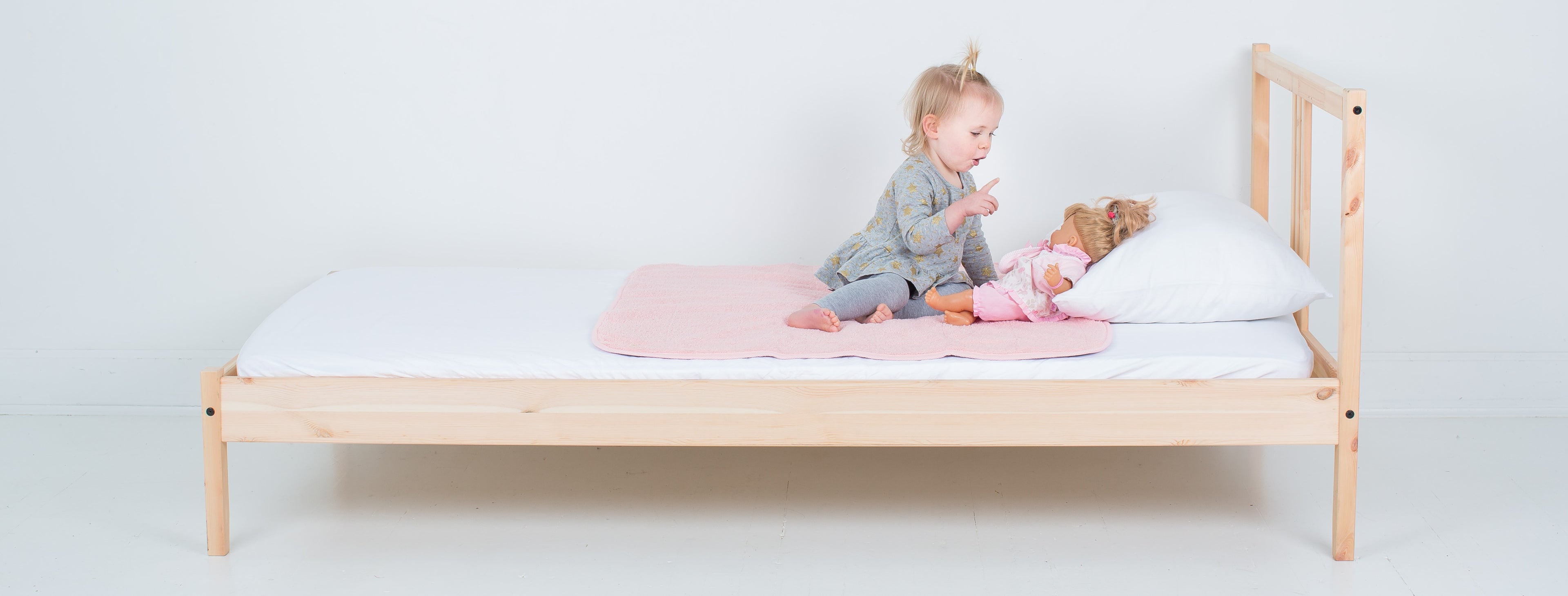 baby girl on bed with doll and peapodmat
