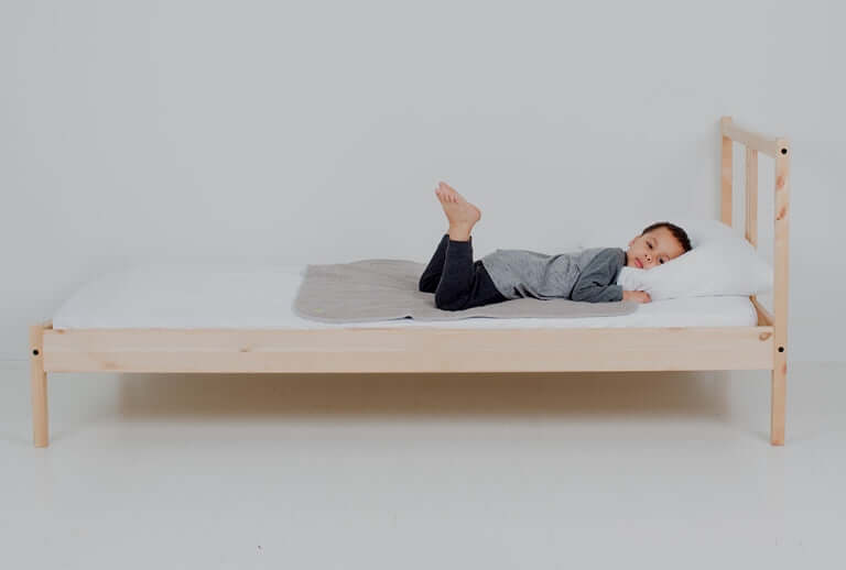 Boy laying on top of medium PeapodMat on a bed