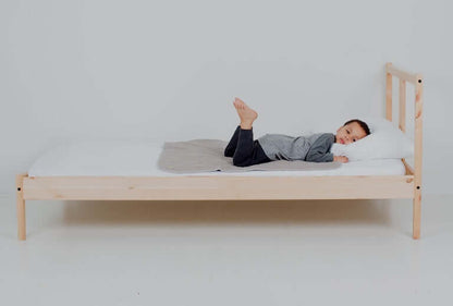 Boy laying on top of medium PeapodMat on a bed